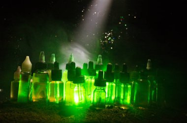 Vape kavramı. Duman bulutları ve vape sıvı şişe koyu arka plan üzerinde. Işık efektleri.