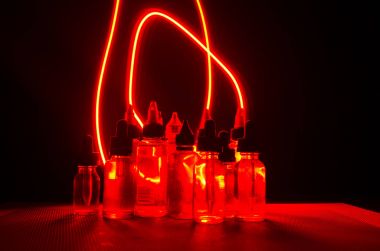 Vape kavramı. Duman bulutları ve vape sıvı şişe koyu arka plan üzerinde. Işık efektleri.