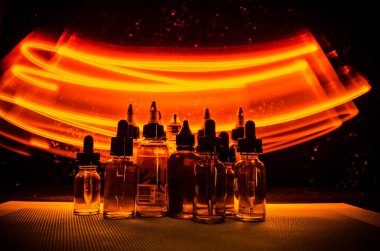 Vape kavramı. Duman bulutları ve vape sıvı şişe koyu arka plan üzerinde. Işık efektleri.