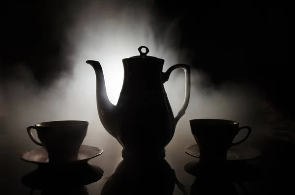 Essen Hintergrund Tee und Kaffee Thema. alte Vintage-Keramik-Tee- oder Kaffeekanne mit Tassen-Kanne und Zuckerbecher auf dunklem Hintergrund mit Licht und Rauch. Silhouetten von Teekanne und Tasse aus Keramik — Stockfoto