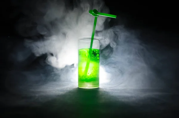 Glas groen cocktail met stro op donkere achtergrond met rook en achtergrondverlichting. — Stockfoto