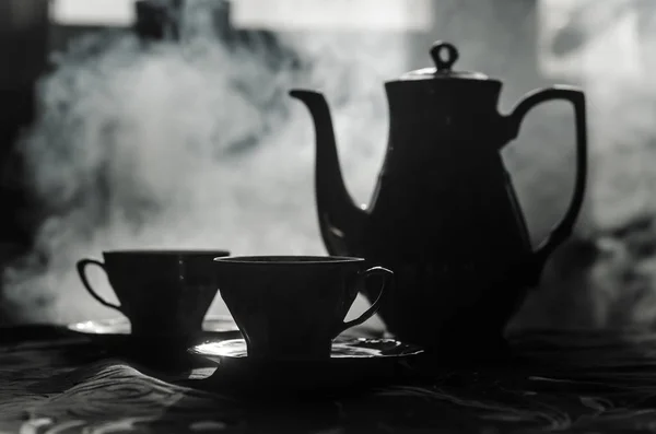 Food background tea and coffee theme. Old vintage ceramic tea or coffee pot with cups jug and sugar cup on dark background with lights and smoke. Silhouettes of ceramic tea pot and cup — Stock Photo, Image