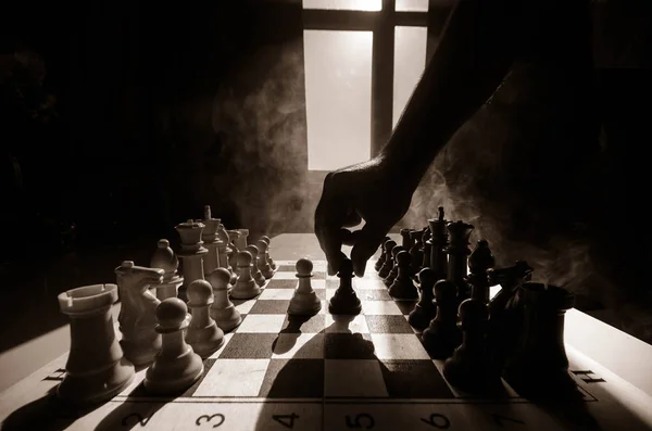 Jeu d'échiquier concept d'idées d'affaires et de la concurrence et des idées de stratégie concéder. Chess figures sur un fond sombre avec de la fumée et du brouillard. Concentration sélective. Main met figure à bord — Photo