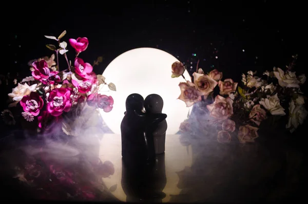 Zwei Puppen umarmen sich auf dem Tisch mit Blumen und Monddekoration beleuchteten Hintergrund mit smoke.love Konzept. Gruß- oder Geschenkkartendesign-Idee. Vintage-Ton. Silhouette eines sich umarmenden Paares — Stockfoto