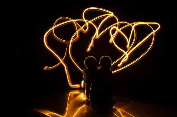 Dois jovens amantes pintam um coração em chamas. Silhueta de casal e palavras de amor em um fundo escuro — Fotografia de Stock