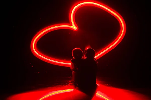 两个年轻的恋人画一颗心在火上。夫妇和爱语在深色背景上的剪影 — 图库照片