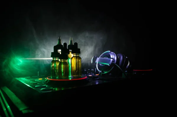 Concepto de Vape y DJ Club. Nubes de humo y botellas de vapor líquido en Dj mezclador de cerca. Efectos de luz. Útil como fondo o publicidad de vapor o club o fondo de vapor . —  Fotos de Stock
