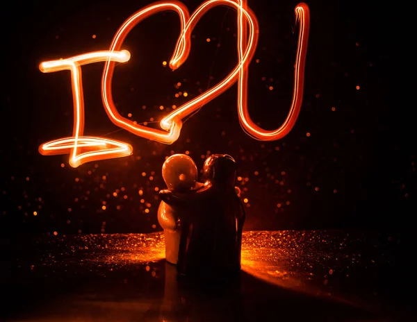 Two young lovers paint a heart on fire. Silhouette of couple and Love words on a dark background — Stock Photo, Image