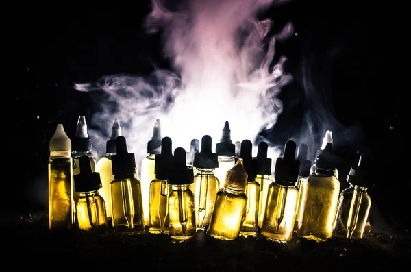 Concepto Vape. Nubes de humo y botellas de vapor líquido sobre fondo oscuro. Efectos luminosos . — Foto de Stock