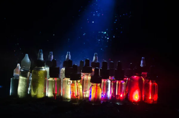 Vape concept. Roken wolken en vape vloeibare flessen op donkere achtergrond. Licht effecten. — Stockfoto