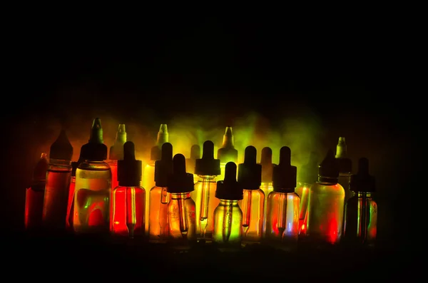 Concepto Vape. Nubes de humo y botellas de vapor líquido sobre fondo oscuro. Efectos luminosos . —  Fotos de Stock