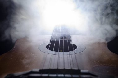 Müzik konsepti. Akustik gitar ile kopya alanı dumanla ışık demeti altında karanlık bir arka plan üzerinde izole. Gitar telleri, yakın çekim. Seçici odak. Yangın etkileri