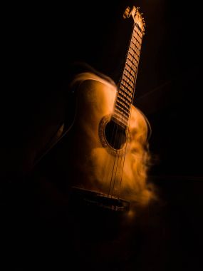 Müzik konsepti. Akustik gitar ile kopya alanı dumanla ışık demeti altında karanlık bir arka plan üzerinde izole. Gitar telleri, yakın çekim. Seçici odak. Yangın etkileri