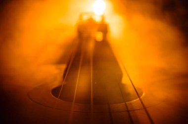 Müzik konsepti. Akustik gitar ile kopya alanı dumanla ışık demeti altında karanlık bir arka plan üzerinde izole. Gitar telleri, yakın çekim. Seçici odak. Yangın etkileri