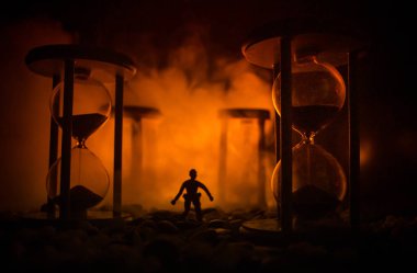 Zaman kavramı. Duman ile hourglasses ve karanlık bir arka plan ışıkları arasında duran bir adam silüeti.