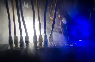 Ağ anahtarı ve ethernet kabloları, global iletişim sembolüdür. Işıklar ve duman ile koyu arka plan üzerinde renkli ağ kabloları. Seçici odak