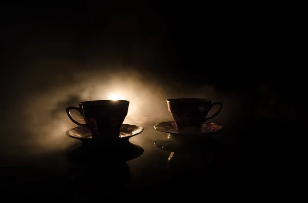 Comida fondo té y café tema. Tetera de cerámica antigua o cafetera con jarra de tazas y taza de azúcar sobre fondo oscuro con luces y humo. Siluetas de tetera y taza de cerámica — Foto de Stock