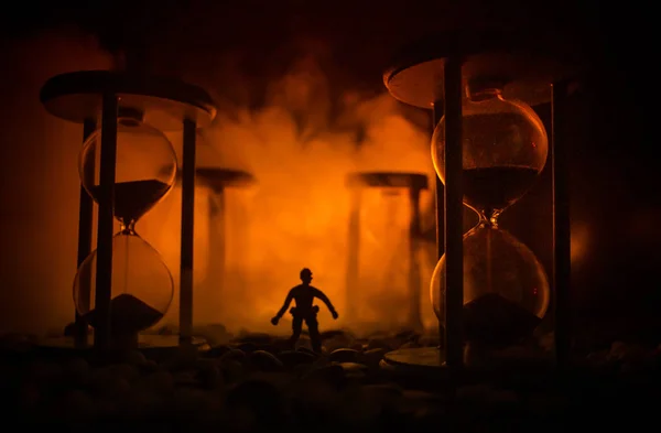 Concepto de tiempo. Silueta de un hombre parado entre clepsidras con humo y luces sobre un fondo oscuro . — Foto de Stock