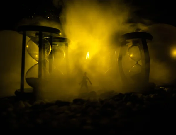 Concepto de tiempo. Silueta de un hombre parado entre clepsidras con humo y luces sobre un fondo oscuro . —  Fotos de Stock