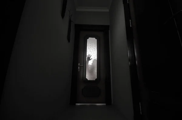 Silueta de una figura de sombra desconocida con las manos en una puerta a través de una puerta de cristal cerrada. Concepto de horror — Foto de Stock