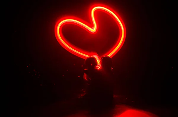 Two young lovers paint a heart on fire. Silhouette of couple and Love words on a dark background — Stock Photo, Image