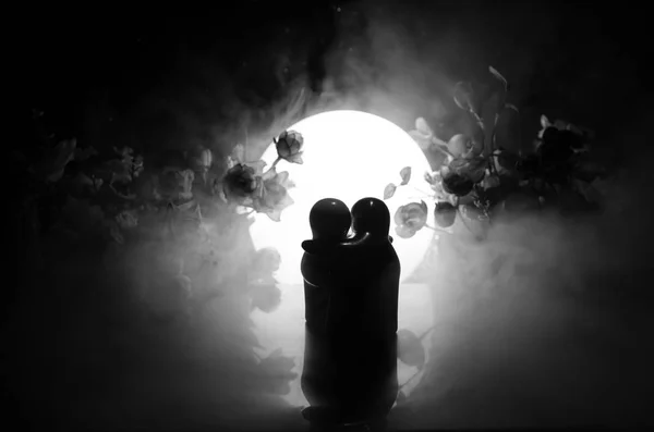 两个娃娃拥抱用鲜花和月亮装饰光背景与烟的桌子上。爱的概念。问候或礼品卡设计理念。老式的口气。拥抱夫妇的剪影 — 图库照片