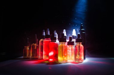 Vape kavramı. Duman bulutları ve vape sıvı şişe koyu arka plan üzerinde. Işık efektleri.