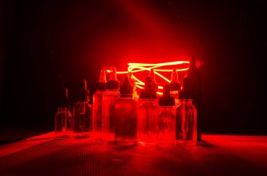 Vape kavramı. Duman bulutları ve vape sıvı şişe koyu arka plan üzerinde. Işık efektleri.