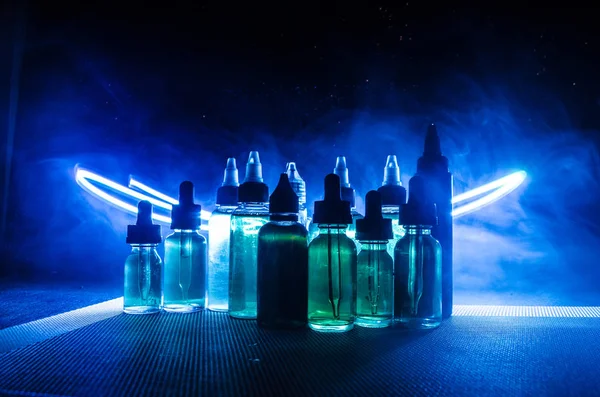 Vape concept. Roken wolken en vape vloeibare flessen op donkere achtergrond. Licht effecten. — Stockfoto