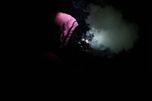 Vaping man holding a mod. Облако паров. Чёрный фон. Изматываю электронную сигарету большим количеством дыма — стоковое фото