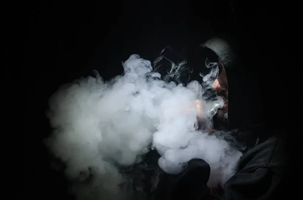 Vaping man holding a mod. Облако паров. Чёрный фон. Изматываю электронную сигарету большим количеством дыма — стоковое фото