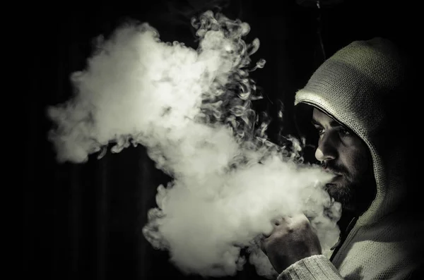 Vaping man holding a mod. A cloud of vapor. Black background. Vaping an electronic cigarette with a lot of smoke — Stock Photo, Image