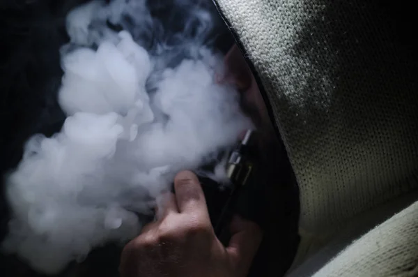 Vaping 男子手持一个 mod。蒸气云。黑色的背景。吸电子烟的大量黑烟与雾 — 图库照片