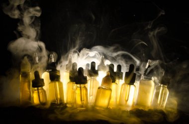 Vape kavramı. Duman bulutları ve vape sıvı şişe koyu arka plan üzerinde. Işık efektleri.