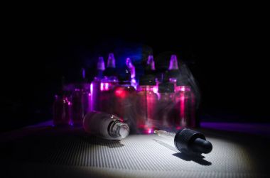 Vape kavramı. Duman bulutları ve vape sıvı şişe koyu arka plan üzerinde. Işık efektleri.