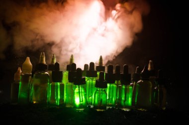 Vape kavramı. Duman bulutları ve vape sıvı şişe koyu arka plan üzerinde. Işık efektleri.