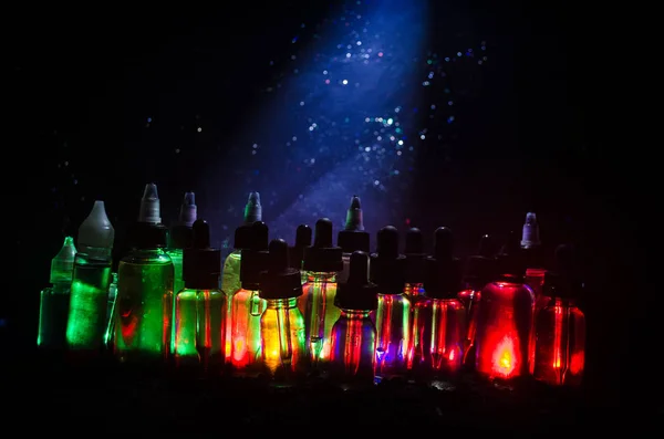 Koncepcja Vape. Pali, chmury i vape płyn butelki na ciemnym tle. Efekty świetlne. — Zdjęcie stockowe