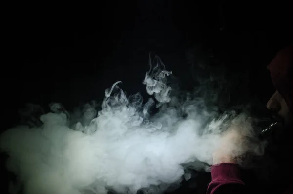 Vaping man holding a mod. A cloud of vapor. Black background. Vaping an electronic cigarette with a lot of smoke — Stock Photo, Image