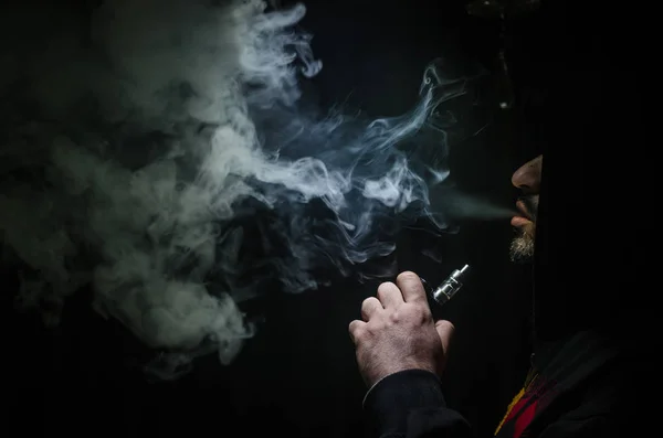 Vaping άνθρωπος που κρατά ένα mod. Ένα σύννεφο των ατμού. Μαύρο φόντο. Ηλεκτρονικό τσιγάρο με πολύ καπνό καπνίσματος — Φωτογραφία Αρχείου