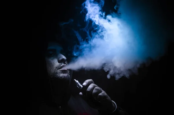 Dampfender Mann mit einem Mod. eine Dampfwolke. schwarzer Hintergrund. Verdampfen einer elektronischen Zigarette mit viel Rauch — Stockfoto