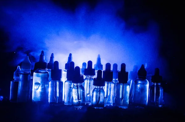 Concepto Vape. Nubes de humo y botellas de vapor líquido sobre fondo oscuro. Efectos luminosos . — Foto de Stock