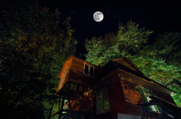 Belle rue de village de paysage avec des bâtiments et des arbres et grande pleine lune au ciel nocturne. Grand Caucase  . — Photo