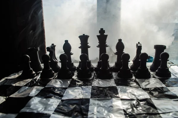 Концепция шахматной настольной игры бизнес-идей, конкуренции и стратегических идей. Шахматные фигуры на темном фоне с дымом и туманом и окном с солнечным светом . — стоковое фото