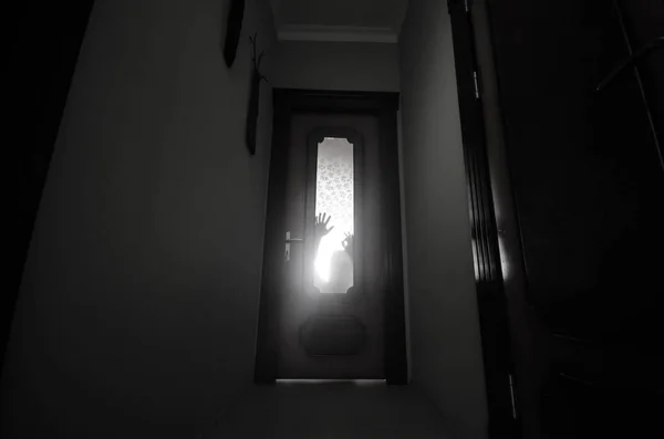 Silueta de una figura de sombra desconocida con las manos en una puerta a través de una puerta de cristal cerrada. Concepto de horror —  Fotos de Stock