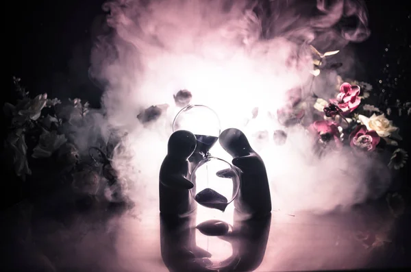 Zwei Puppen umarmen sich auf dem Tisch mit Blumen und Monddekoration beleuchteten Hintergrund mit smoke.love Konzept. Gruß- oder Geschenkkartendesign-Idee. Vintage-Ton. Silhouette eines sich umarmenden Paares — Stockfoto