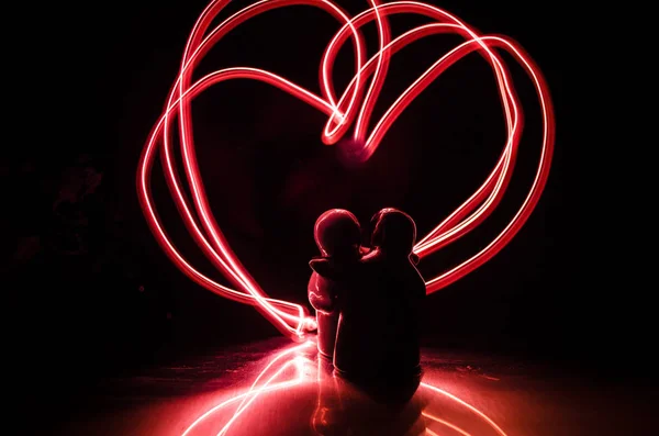 Zwei junge Liebende malen ein Herz in Flammen. Silhouette eines Paares und Liebesworte auf dunklem Hintergrund — Stockfoto