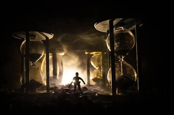 Concept du temps. Silhouette d'un homme debout entre des sabliers avec de la fumée et des lumières sur un fond sombre . — Photo