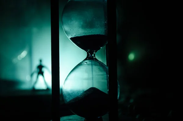 Zaman kavramı. Duman ile hourglasses ve karanlık bir arka plan ışıkları arasında duran bir adam silüeti. — Stok fotoğraf