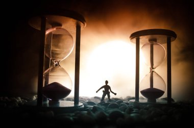 Zaman kavramı. Duman ile hourglasses ve karanlık bir arka plan ışıkları arasında duran bir adam silüeti.