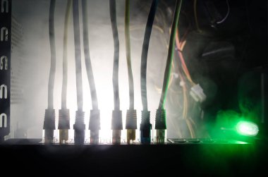 Ağ anahtarı ve ethernet kabloları, global iletişim sembolüdür. Işıklar ve duman ile koyu arka plan üzerinde renkli ağ kabloları. Seçici odak